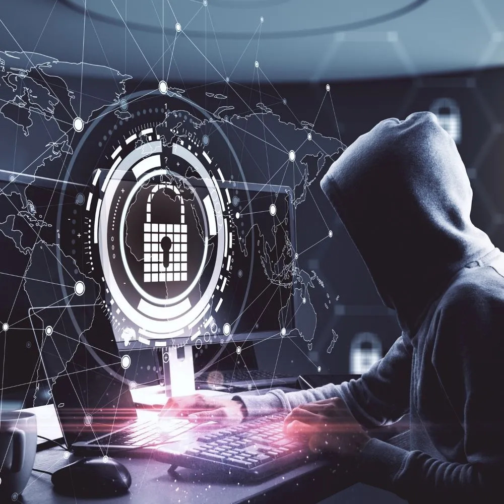 Hooded figure at a computer with a cybersecurity lock interface